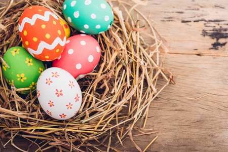 Beautiful Easter multi color egg in straw on wooden background, Easter day conceptの写真素材