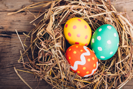 Beautiful Easter multi color egg in straw on wooden background, Easter day conceptの写真素材