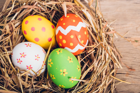 Beautiful Easter multi color egg in straw on wooden background, Easter day conceptの写真素材