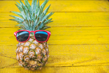 Holiday pineapple have sunglasses on yellow  wooden background, tropical holiday conceptの写真素材
