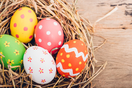 Beautiful Easter multi color egg in straw on wooden background, Easter day conceptの写真素材