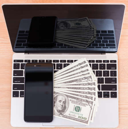 Top view laptop computer, dollar bill and smartphone blank screen on office desk table, finance conceptの写真素材