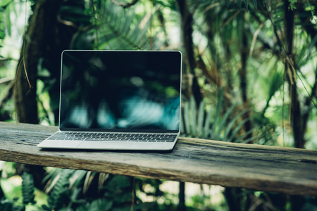 Laptop computer mockup has empty screen outside on table in garden of coffee shopの写真素材