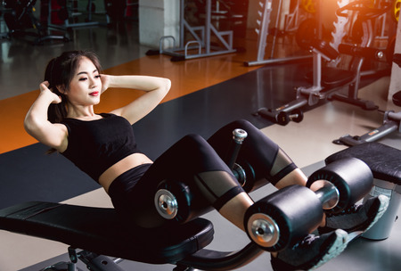 Young beautiful woman training using equipment machine abs sit up workout at fitness gymの写真素材
