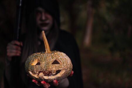 Woman ghost horror her have scythe and pumpkin on hand in forest, halloween day conceptの写真素材