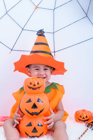 Funny happy kid in Halloween costume with pumpkin Jack with Cobweb on backgroundの写真素材