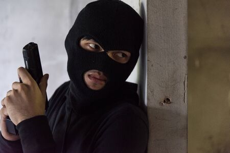 Man robber thief wear mask holding gun hiding armed waiting criminalの写真素材