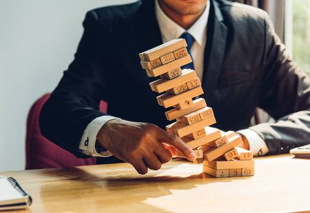Business man challenge pulling block wood building tower, the block wood has falling on he hand, risk conceptの写真素材