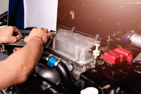 Professional car repair or maintenance mechanic engine working service with laptop computer at...