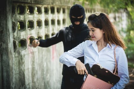 The black man robbers are about to criminal rob woman with a knife. But the woman fixes hide her gun in bag money of her.の写真素材