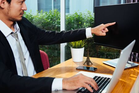 Businessman using laptop computer on desk point hand to PC monitor