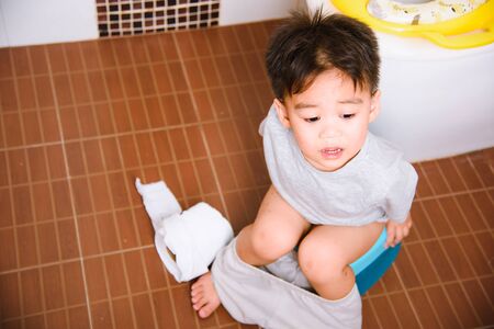 Asian little  kid 2-3 years old sitting on a kid bathroom accessory toilet and he play papers...