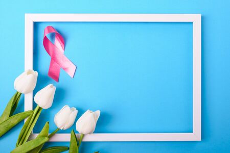 Breast cancer month concept, flat lay top view, pink ribbon and Tulip Flower with photo frame on blue background with copy space for your textの写真素材