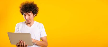 Asian handsome man with curly hair using laptop computer isolate on yellow background with copy...