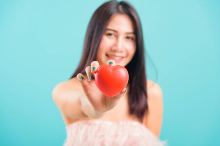 Portrait asian beautiful woman smiling her Stick out red heart on hand focus heart on blue background, with copy space for textの写真素材