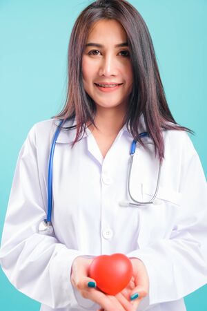 Portrait asian beautiful doctor woman smiling her standing with stethoscope holding heart on blue background, with copy space for textの写真素材