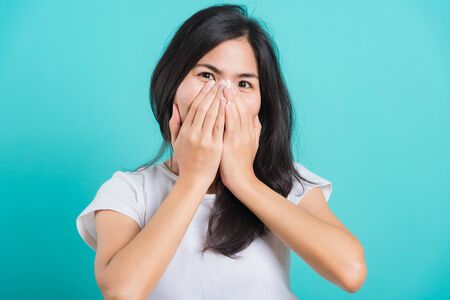Portrait Asian beautiful happy young woman wear t-shirt happy excited laughs covering mouth with hands, on a blue background, with copy spaceの写真素材