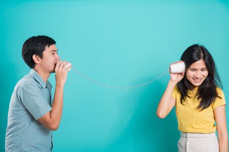 Asian happy young couple beautiful handsome smile and talking together with paper can telephone in a studio shot on blue background with copy space for textの写真素材