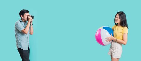 Happy Asian young beautiful woman handsome man couple in summer in holiday travel beach accessories ball and camera isolated on blue background with copy space for textの写真素材