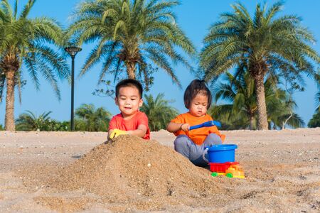 Asian Thai happy cute little cheerful Brother and sister two children funny digging play toy with sand at an outdoor tropical beach in summer day with copy spaceの写真素材