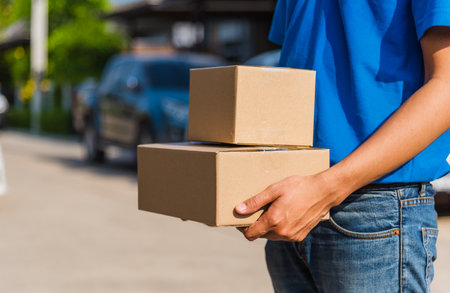 Asian Young delivery man courier online with box in blue cap and t-shirt uniform he protective face...
