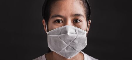 Closeup Asian young woman wearing protective face mask with fear in the eye, prevent germs or disease hygiene prevention COVID-19 virus or coronavirus protection concept, dark on black backgroundの写真素材