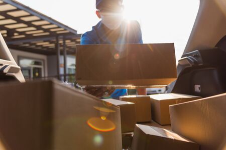 Asian delivery man courier moving deliveries out boxes in back car he protective face mask, service customer on front house under curfew quarantine pandemic coronavirus COVID-19, in car trunk viewの写真素材