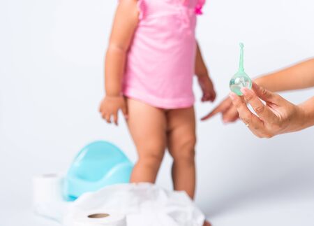 Asian little cute baby child girl training to sitting on blue chamber pot or potty her problem cannot shit and mother use Enema for help, studio shot isolated on white background, wc toilet conceptの写真素材