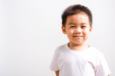 Closeup face Asian Thai portrait happy cute little child boy smiling wearing t-shirt he looking to camera, studio shot, isolated on white background with copy spaceの写真素材