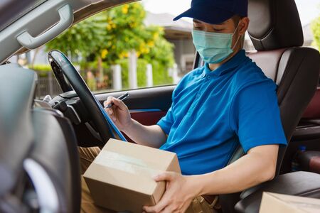 Asian delivery courier young man driver inside the van car with parcel post boxes checking amount he protective face mask, under curfew quarantine pandemic coronavirus COVID-19の写真素材