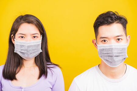 Asian beautiful woman and handsome man wearing protection face mask against coronavirus, looking to camera, studio shot isolated on yellow background with copy space, COVID-19 or corona virus conceptの写真素材