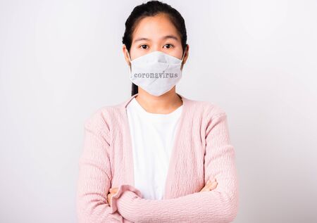 Asian beautiful woman wearing protection face mask against coronavirus standing crossed arm, studio shot isolated on white background with copy space, COVID-19 or corona virus conceptの写真素材