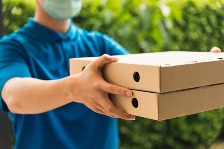 Asian young delivery man courier sending and holding fast food pizza boxed in uniform he protective...