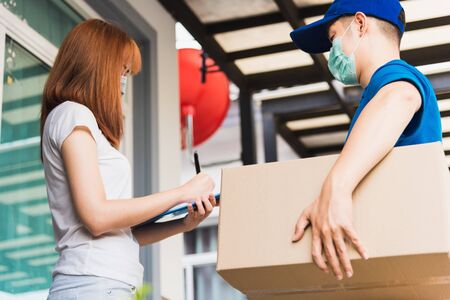 Asian young delivery man courier shopping online with package post box in uniform protective face...