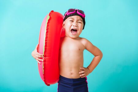 Summer vacation concept, Portrait Asian happy cute little child boy wear goggles and swimsuit hold watermelon inflatable ring, Kid having fun on summer vacation, studio shot isolated blue backgroundの写真素材