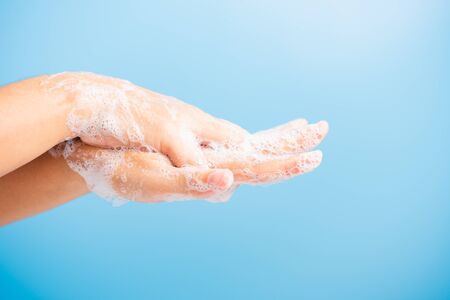 Closeup body care Asian young woman washing hands with soap have foam, hygiene prevention COVID-19 or coronavirus protection concept, isolated on blue backgroundの写真素材