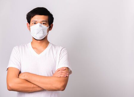 Closeup Asian handsome Man wearing surgical hygienic protective cloth face mask against coronavirus and stand crossed arm, studio shot isolated white background, COVID-19 medical conceptの写真素材