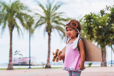 Happy Asian funny child or kid little girl smile wear pilot hat and goggles play toy cardboard...