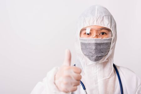 Asian female woman doctor or nurse in PPE uniform and gloves wearing face mask protective in laboratory holding show finger thumb up for good sign, Health medical coronavirus or COVID-19 conceptの写真素材