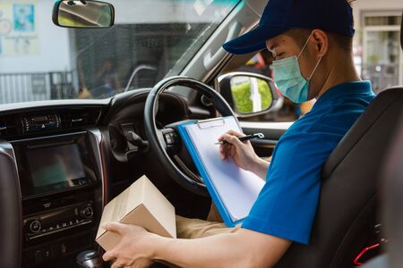 Asian delivery courier young man driver inside the van car with parcel post boxes checking amount he protective face mask, under curfew quarantine pandemic coronavirus COVID-19の写真素材