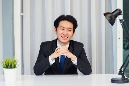 Work from home, Close up face of Asian young businessman video conference call or facetime he looking to camera sitting and holding hands to listen to colleagues explain the work on desk at officeの写真素材