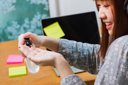 Asian young business woman wearing face mask protective working from home office with laptop computer he quarantines disease coronavirus or COVID-19 and cleaning hands with sanitizer alcohol gel pumpの写真素材