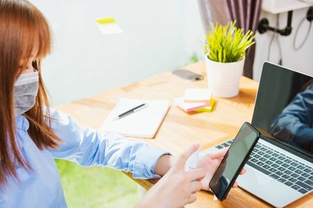 Asian young business woman wearing face mask protective working from home office with laptop...