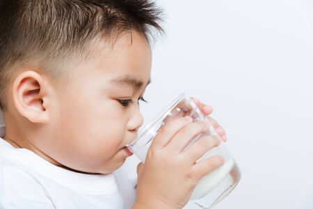 Close up of happy Asian little cute child boy hand holding milk glass he drinking white milk during sitting on the sofa at home after lunch. Daily life health care Medicine foodの写真素材