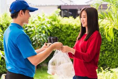Asian young delivery man in blue uniform he making grocery service giving rice food boxes plastic bags to woman customer receiving front house under pandemic coronavirus, Back to new normal conceptの写真素材