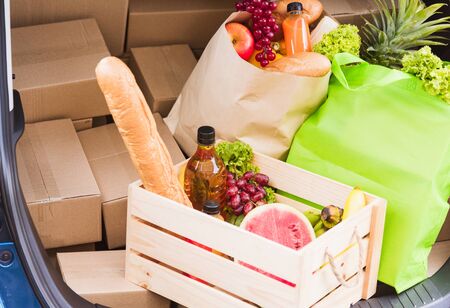 Grocery service giving fresh vegetables and fruits and food in green cloth bag and wooden basket on the back car ready delivery to send woman customerの写真素材