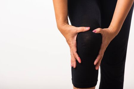 Closeup young woman aches to suffer from pain knee and she uses hand joint hold knee agony, studio...