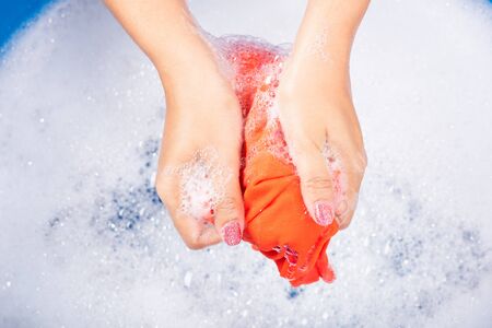 Closeup young Asian woman use hands washing color clothes in basin with detergent have soapy bubble water, studio shot background, laundry conceptの写真素材
