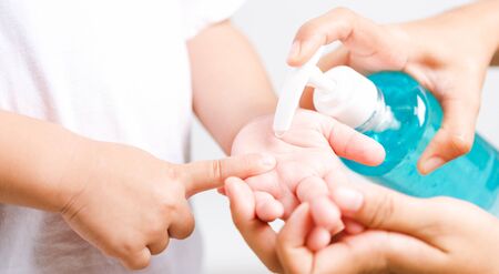 Closeup Asian Mother applying bottle pump dispenser sanitizer alcohol gel cleaning washing hands little child boy COVID-19 or coronavirus protection concept, isolated white background with copy spaceの写真素材