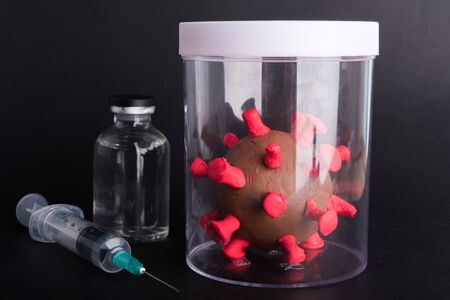 Imprison prevent plasticine disease cells virus in bottle, vaccine and syringe for research in lab of coronavirus outbreak and coronaviruses influenza flu, isolated on black, COVID-19 medical conceptの写真素材